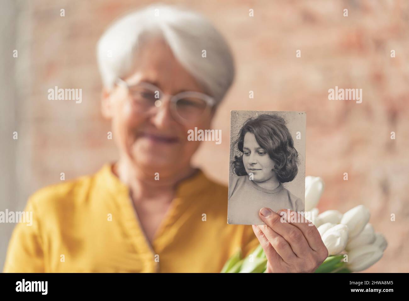 Ältere ältere ältere ältere kaukasische Frau im Ruhestand, die Kamera konzentriert sich auf das Schwarz-Weiß-Foto ihrer jüngeren Version. Hochwertige Fotos Stockfoto