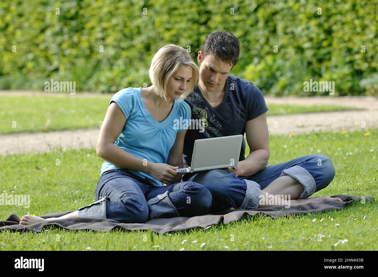 Das junge Paar sitzt barfuß auf einer Wiese und liest zusammen in einem Laptop Stockfoto