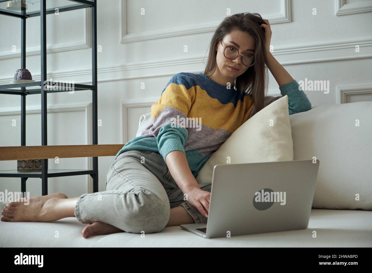 Junge Frau mit Laptop, tippen, Touchpad verwenden, zu Hause auf dem Sofa sitzen, fernarbeiten, zu Hause arbeiten Stockfoto