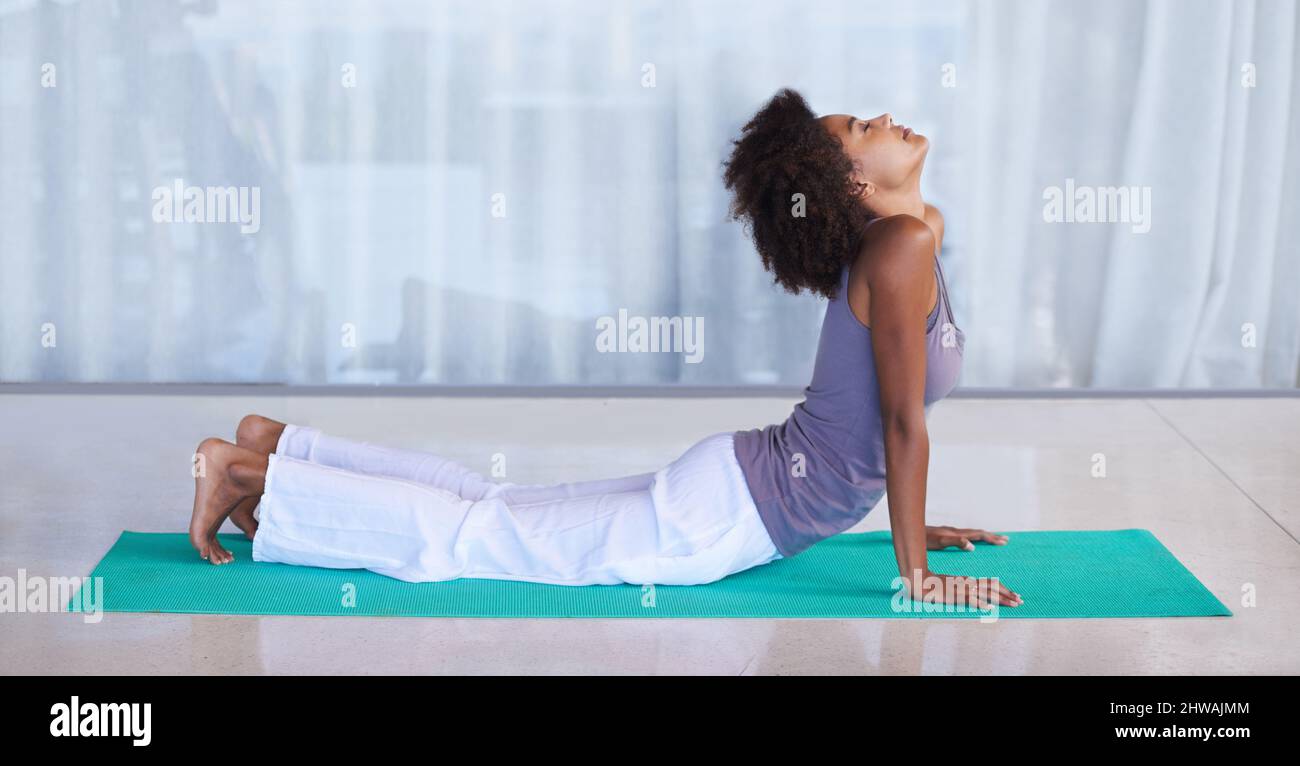 Streckt ihren Rücken aus. Aufnahme einer attraktiven jungen Frau, die auf einer Trainingsmatte Yoga macht. Stockfoto