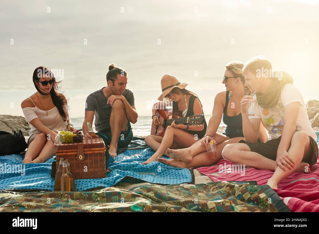 Unsere besten Erinnerungen werden am Strand gemacht. Aufnahme einer Gruppe glücklicher junger Freunde, die gemeinsam ein Picknick am Strand genießen. Stockfoto