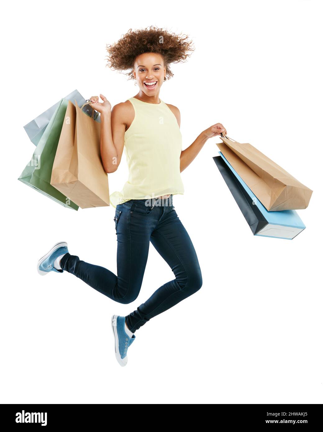 Genuss am Zahltag. Studioportrait einer aufgeregten jungen Frau, die Einkaufstaschen trägt und vor Freude vor weißem Hintergrund springt. Stockfoto