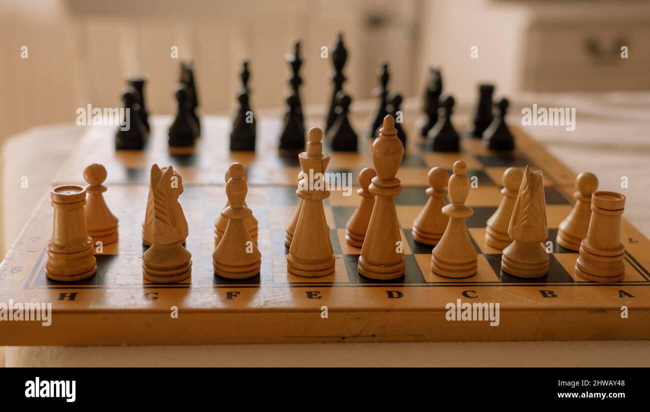 Hölzerne Schachfiguren stehen in einer Reihe auf einem alten Schachbrett Anfang des Spiels. Stockfoto