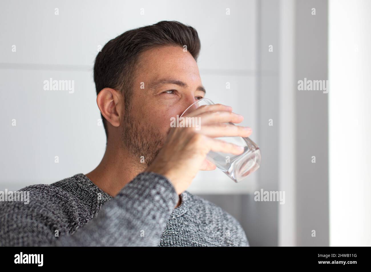 Der Mann trinkt drinnen Wasser aus dem Glas und schaut weg Stockfoto