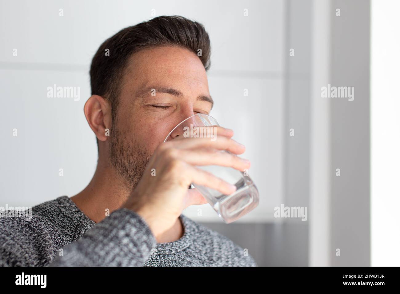 Der Mann trinkt drinnen Wasser aus Glas, die Augen geschlossen Stockfoto