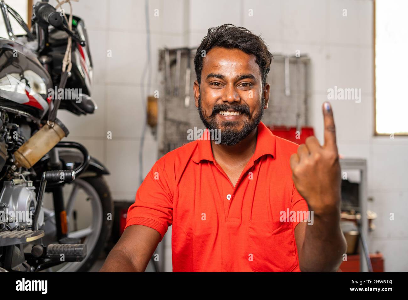 Glücklicher lächelnder Mechaniker, der nach der Abstimmung bei der Wahl einen mit Tinte markierten Wählerfinger zeigte - Konzept von Verantwortung, Demokratie und Recht Stockfoto