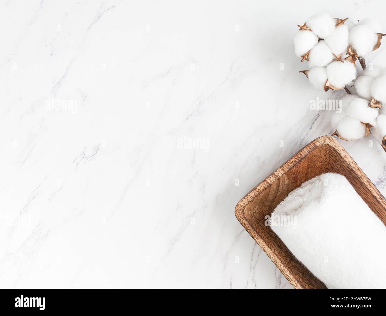Minimale Spa-Hintergrund oder Dekor Zusammensetzung für Werbung, Abdeckung. Baumwollhandtücher auf Holztablett und Baumwollzweig auf weißem Marmorhintergrund. Flach liegend. Stockfoto