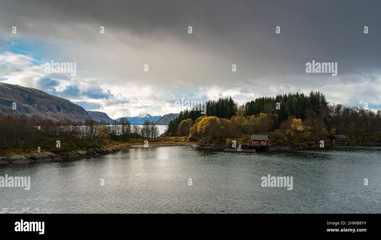 rotes Haus an der Küste von Norwegen bei Ørnes, an einer einzigen, ruhigen Stelle, umgeben von herbstlich gestärkten Bäumen im Morgenlicht Stockfoto