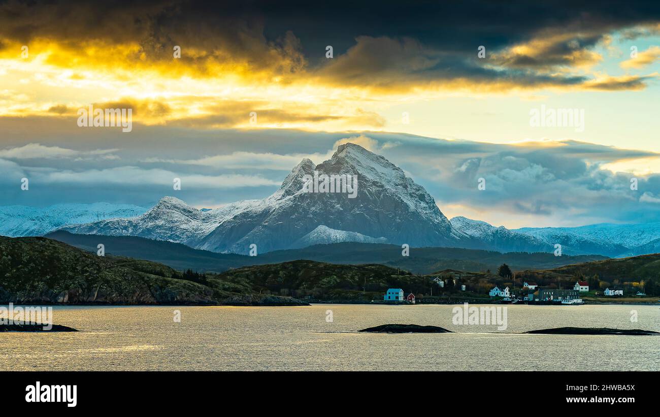 Vom Sonnenaufgang orange verstärkte Wolken über den frisch verschneiten Bergen der Küste von Norwegen, zwischen Nesna und Ørnes im Nordland. Stockfoto