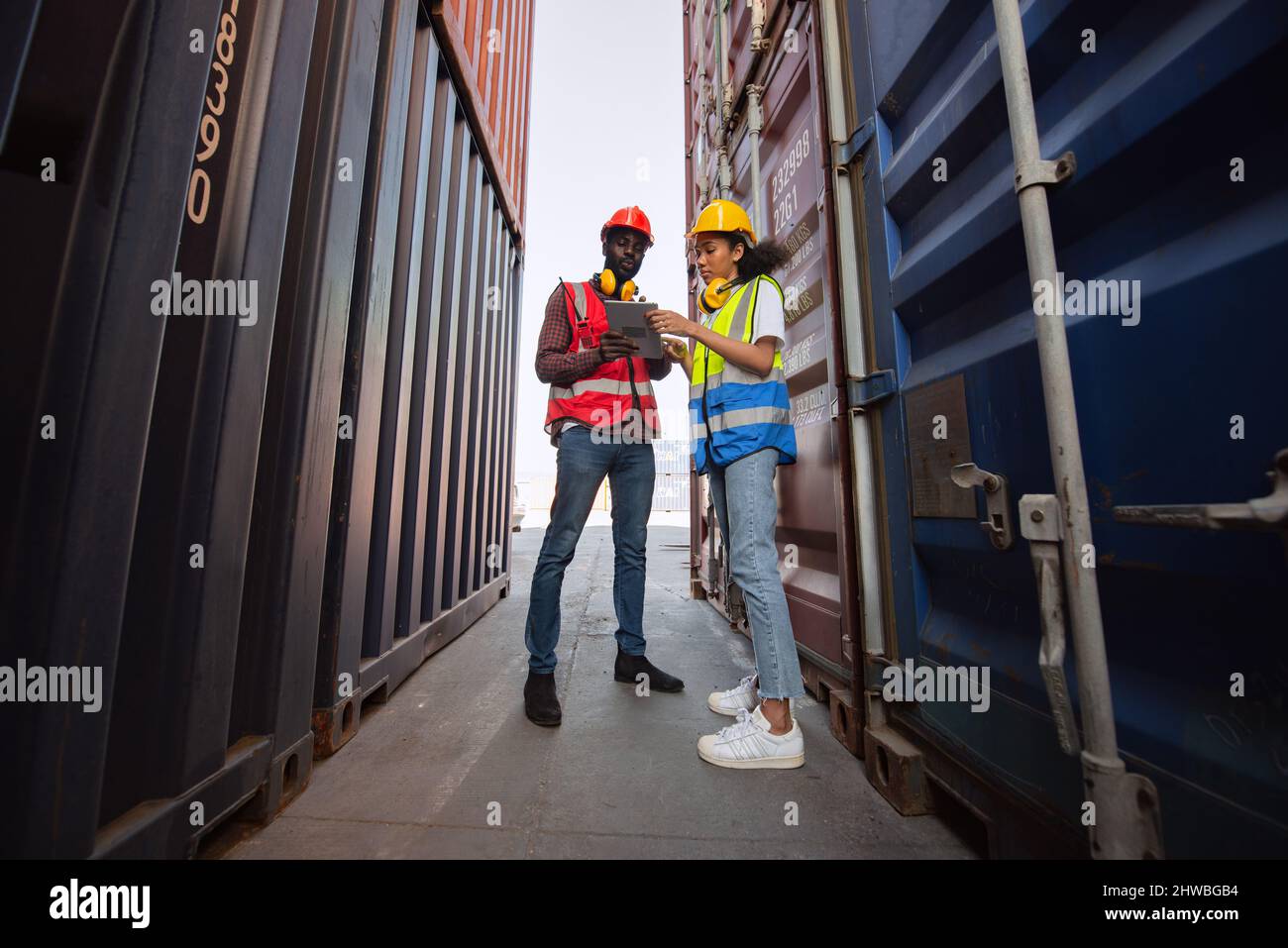 Zwei afroamerikanische Arbeiter, die Tablet-PCs benutzen und kontrollieren, ob Frachtcontainer vom Frachtschiff für den Import geladen werden. Stockfoto