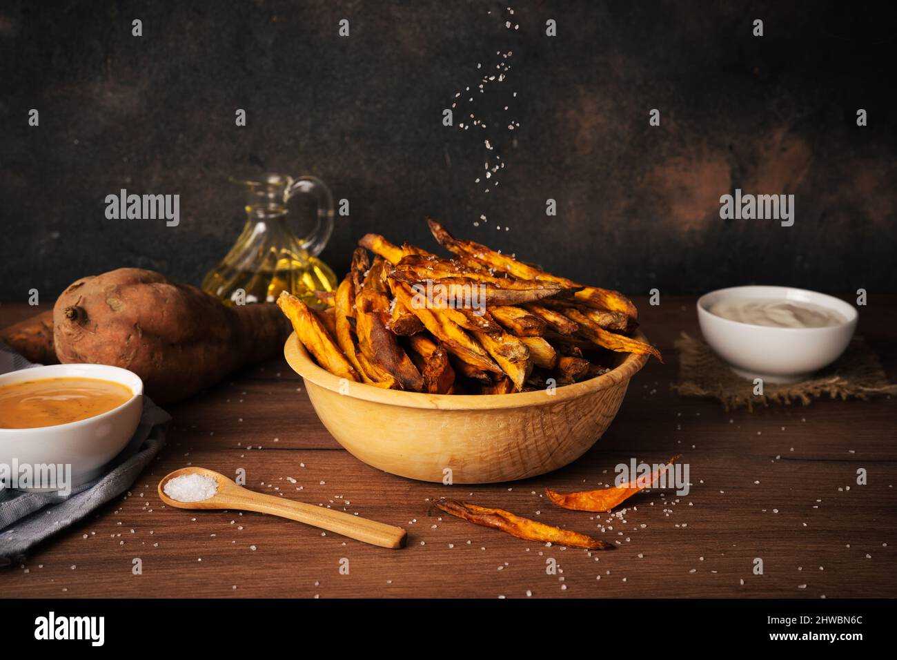 Köstliche und gesunde hausgemachte Süßkartoffelfrites, die in einer Luftfryer mit Saucen auf dunklem rustick-Hintergrund zubereitet werden Stockfoto