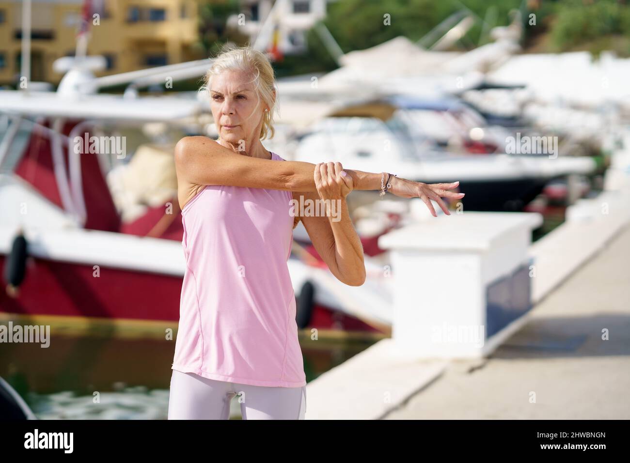 Eine ältere Sportlerin, die die Arme im Hafen streckt, sitzt Stockfoto