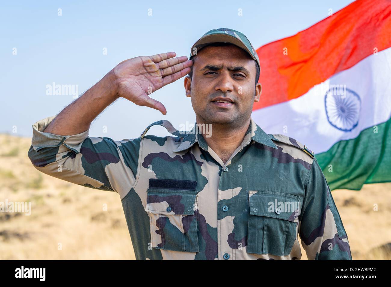 Armeeoffizier grüsst mit Blick auf die Kamera vor der winkenden indischen Flagge - ein Gespann von Patriotismus, Respekt und Stolz. Stockfoto