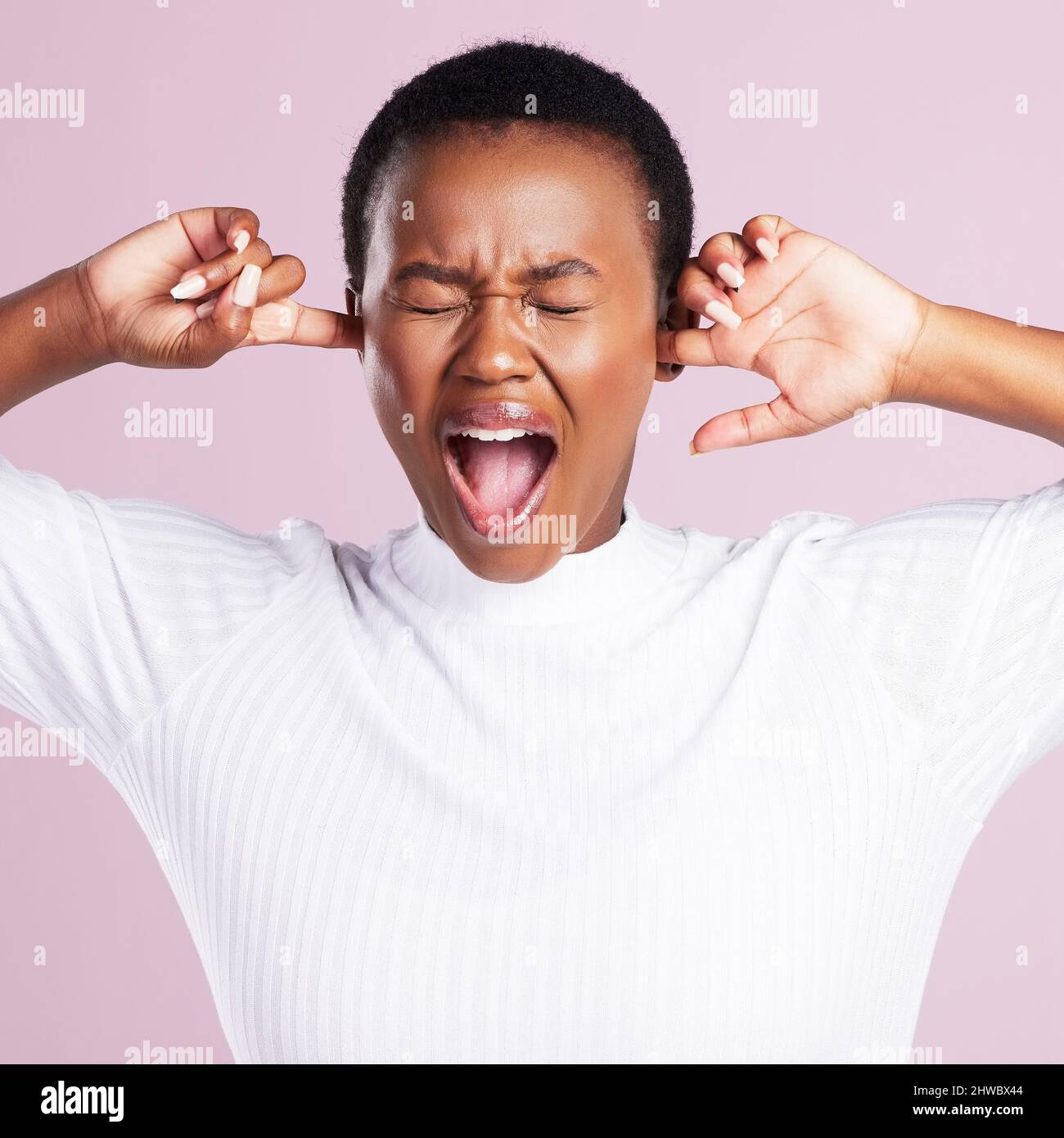 Die Negativität zu blockieren. Studioaufnahme einer jungen Frau, die ihre Finger hält, um ihre Ohren vor einem rosa Hintergrund zu schließen. Stockfoto