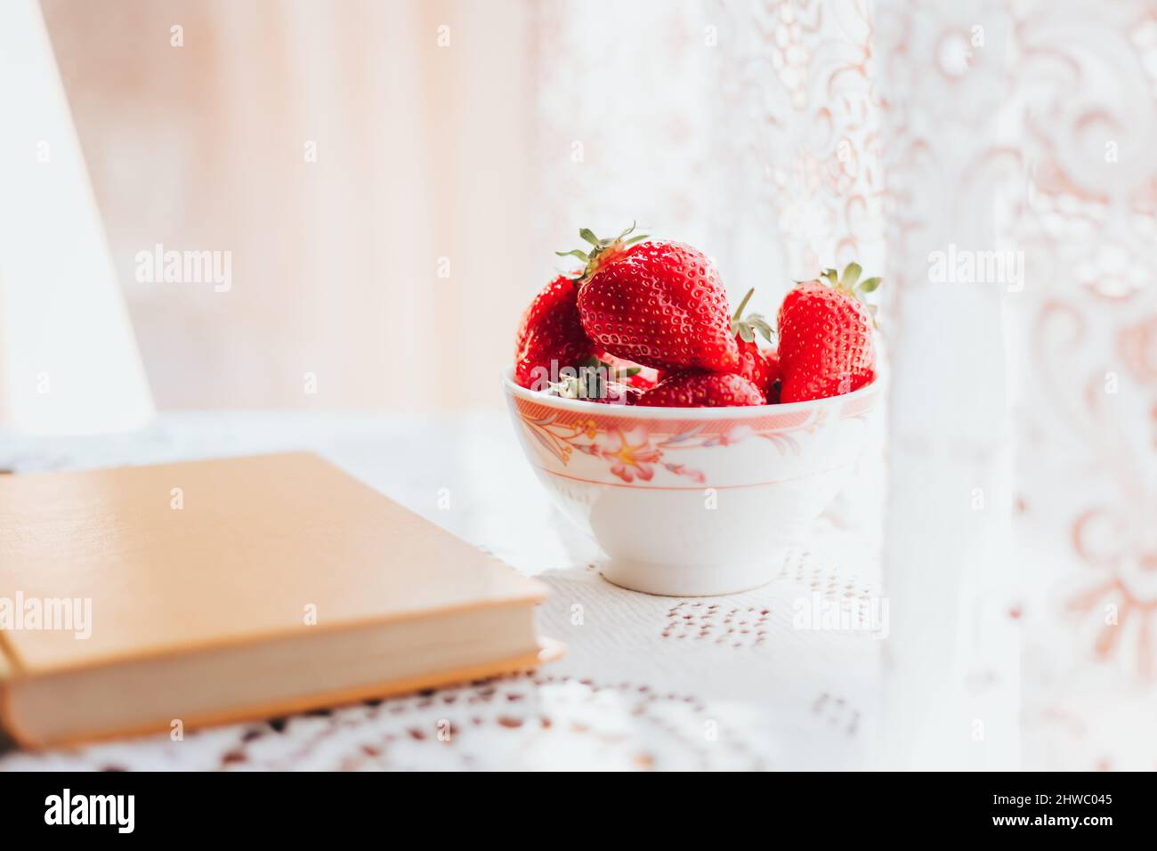 Frische Erdbeeren im Keramiktuch auf dem Tisch und ein Buch. Freizeit am Morgen Stockfoto