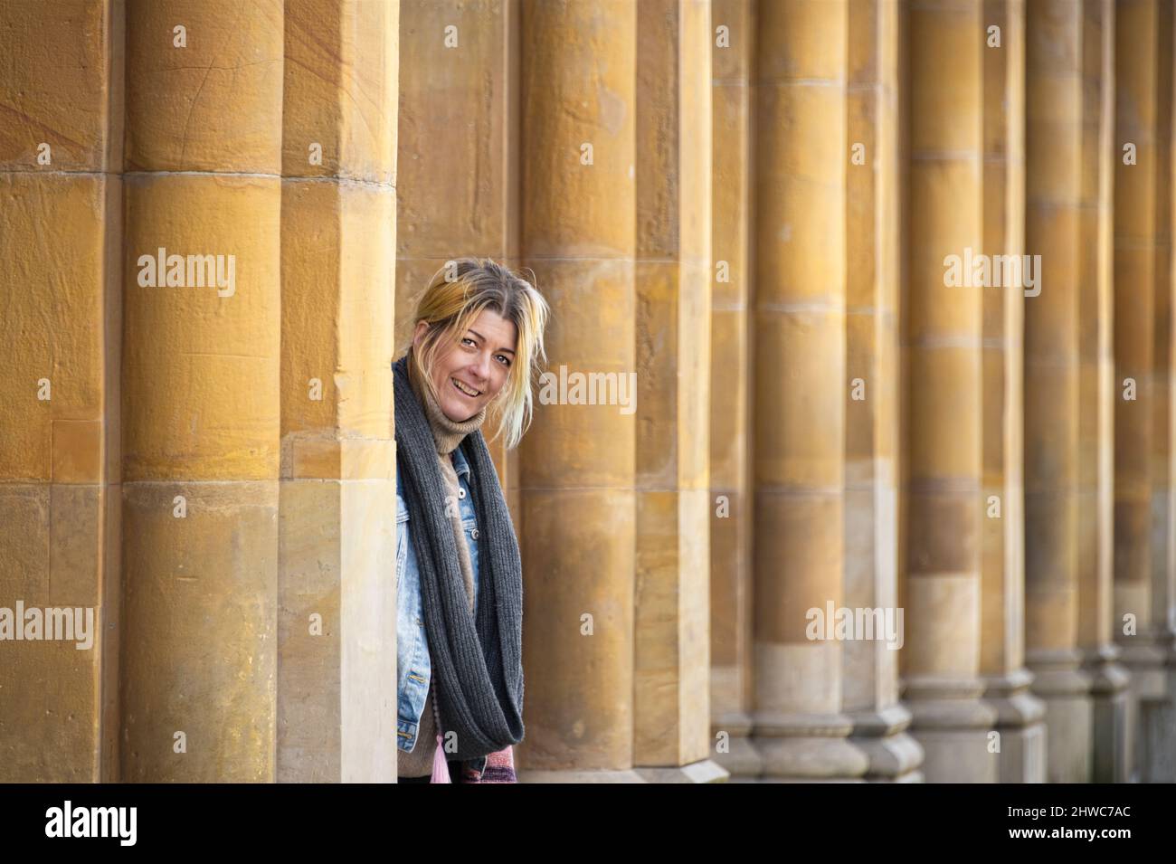 Blonde europäerin lächelt und blickt auf die Kamera gegen die gelben Säulen eines Gebäudes Stockfoto