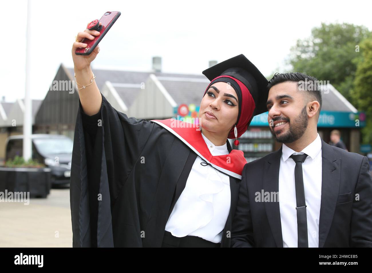 Eine asiatische Absolventin posiert mit ihrem Partner bei ihrer Abschlussfeier für Fotos. Dieses formelle Ereignis, bei dem sich die Graduierung (vor) ändert Stockfoto