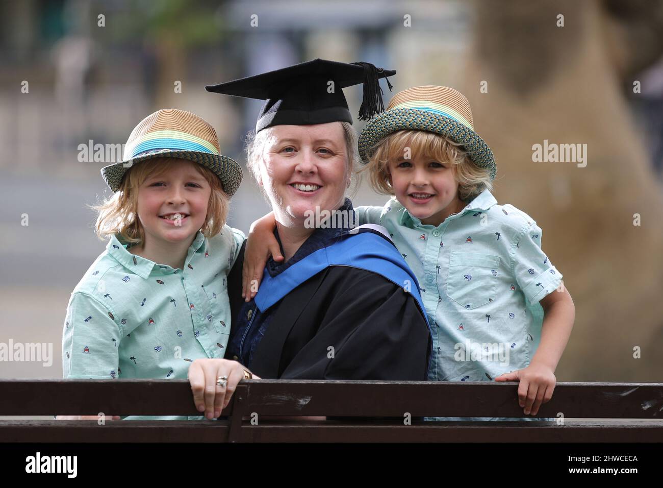 Eine europäische Absolventin posiert für Fotos mit ihren blonden Söhnen bei ihrer Abschlussfeier. Dieses formelle Ereignis, bei dem die Graduierung (vor) Cha Stockfoto