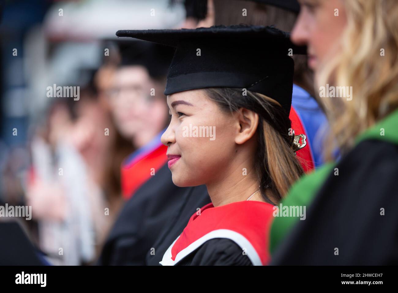 Eine hübsche asiatische Absolventin steht bei ihrer Abschlussfeier mit ihren Kommilitonen an. Dieses formelle Ereignis, bei dem sich die Graduierung (vor) ändert Stockfoto