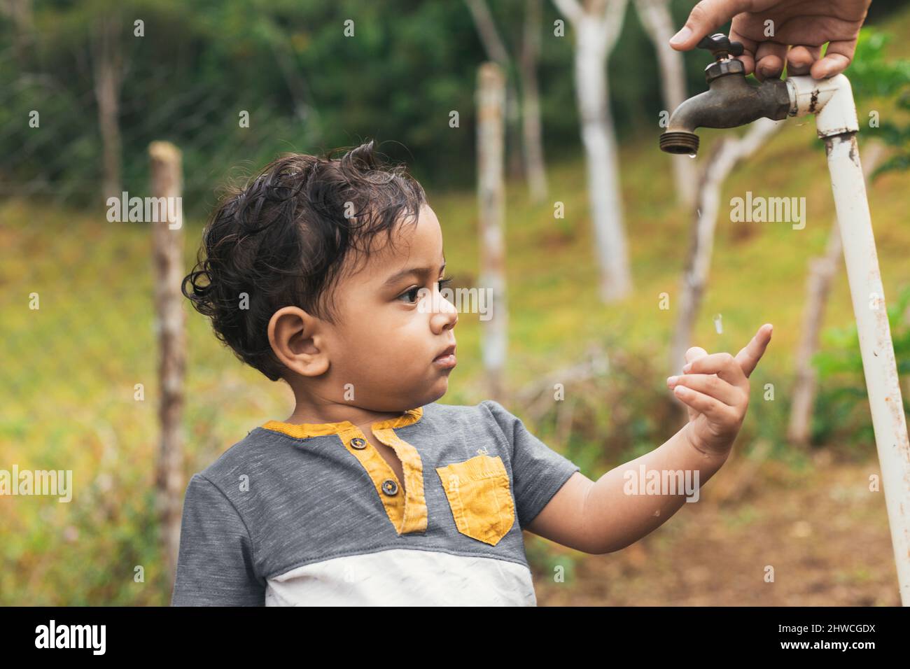 Lateinischer Junge, der die Wassertropfen berührt, die aus dem Wasserhahn kommen, trinkt mit dem Finger auf das Wasser zeigend Stockfoto