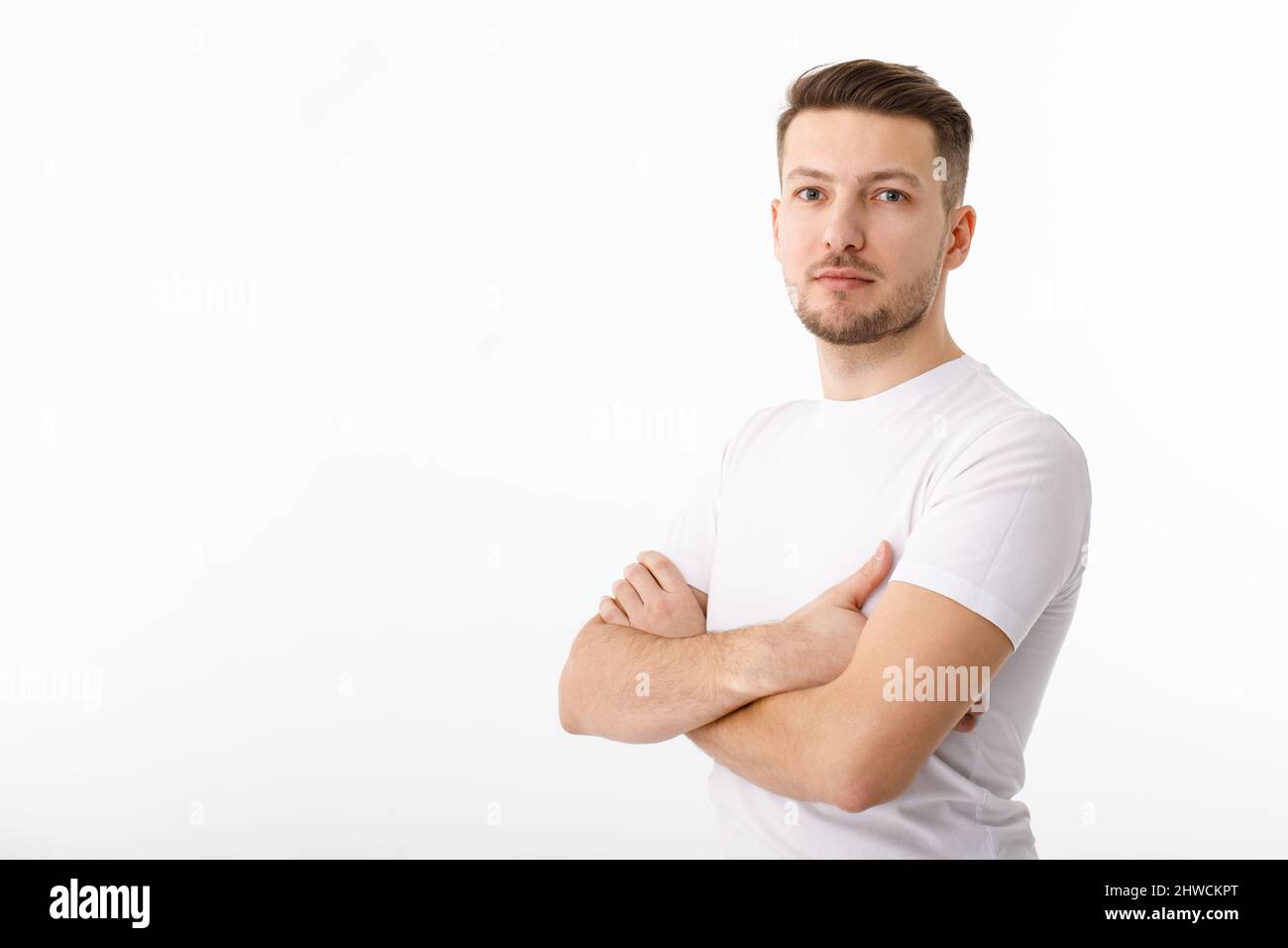 Porträt eines fröhlichen jungen Mannes in einem weißen T-Shirt auf weißem Hintergrund. Der Typ steht und schaut auf die Kamera und lächelt. Stockfoto