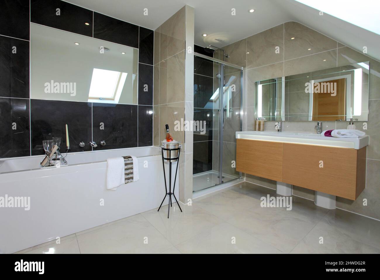 Badezimmer mit Waschbecken für Sie und ihn, Dusche und Champagner auf einem Ständer neben der Badewanne. Stockfoto