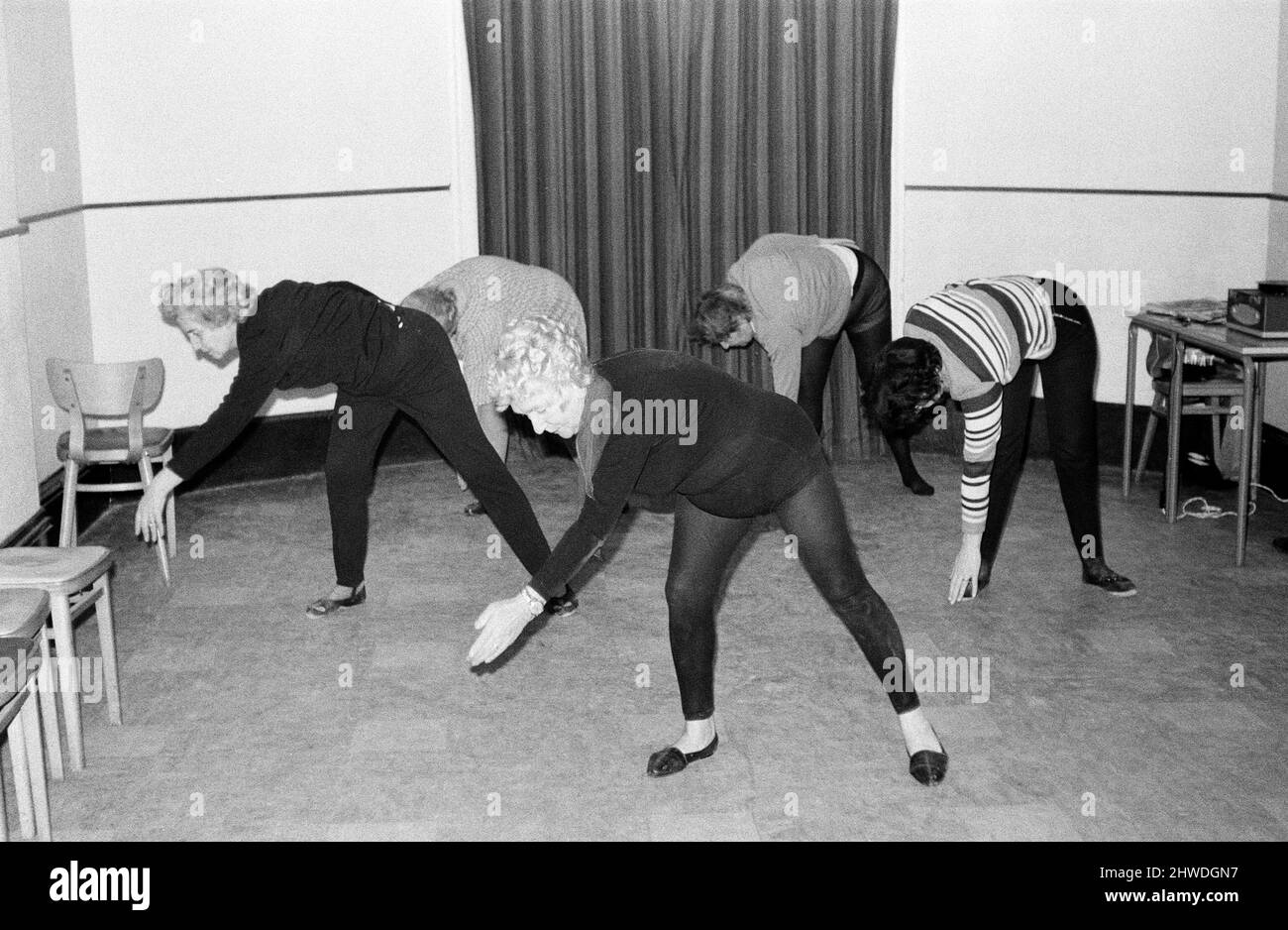 Cornwalls erstaunlichste Großmutter, Mrs Mary Wyatt (75 im April nächsten Jahres), tanzt sich in das neue Jahrzehnt der 1970s, bekleidet mit schwarzen Tanzstrumpfhosen, die einer Klasse von Frauen zeigen, wie sie energische und athletische Arm- und Beinstrecken zur Musik machen. Frau Wyatt hielt ihre erste Keep Fit-Klasse der 1970s in den Gemeinschaftsräumen im Guildhall in St. Ives, Cornwall. 2.. Januar 1970.Cornwalls erstaunlichste Großmutter, Mrs Mary Wyatt (75 im April nächsten Jahres), tanzt sich in das neue Jahrzehnt der 1970s, bekleidet mit schwarzen Tanzstrumpfhosen, die einer Klasse von Frauen zeigen, wie sie energische und athletische Arm- und Beinstrecken bis zum Mus machen Stockfoto