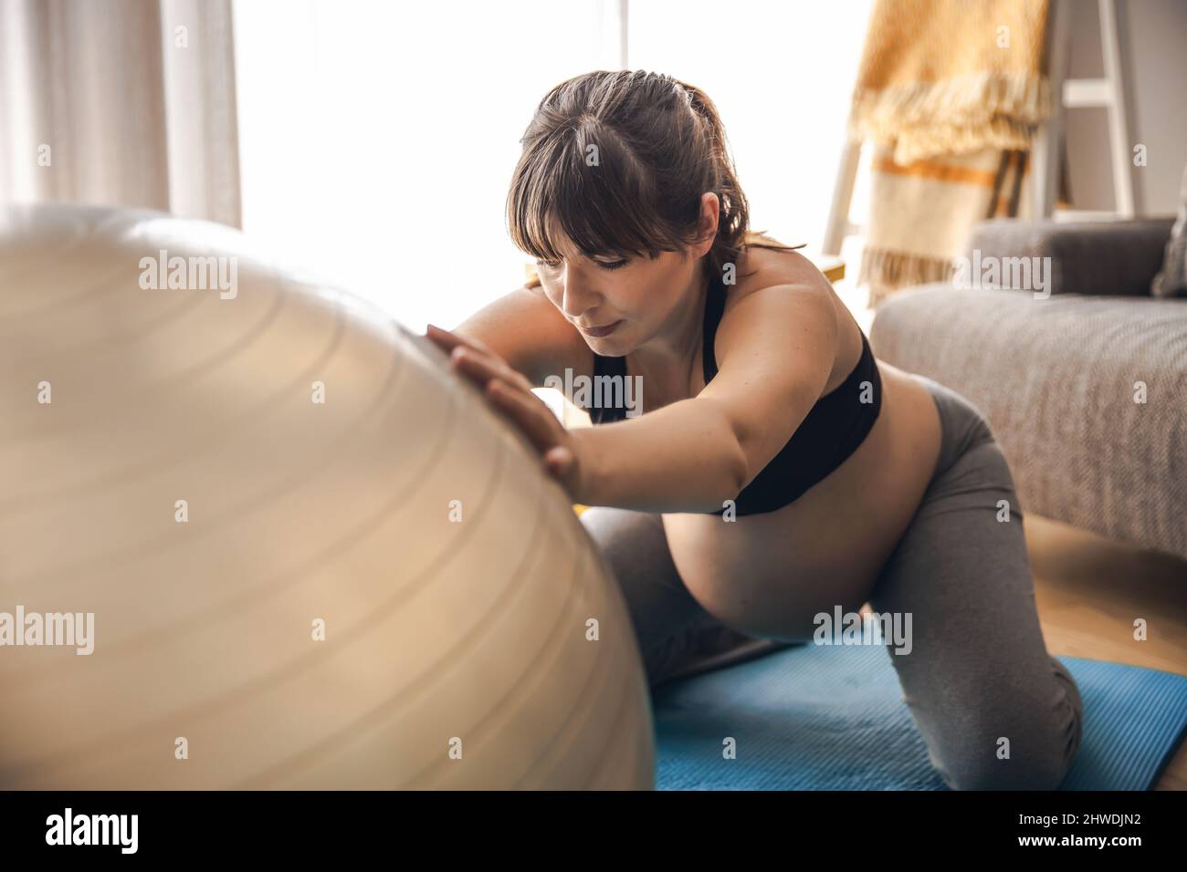 Eine Schwangerin, die zu Hause trainiert und Übungen auf einem Fitball macht. In guter Form bleiben, während Sie auf das Baby warten Stockfoto