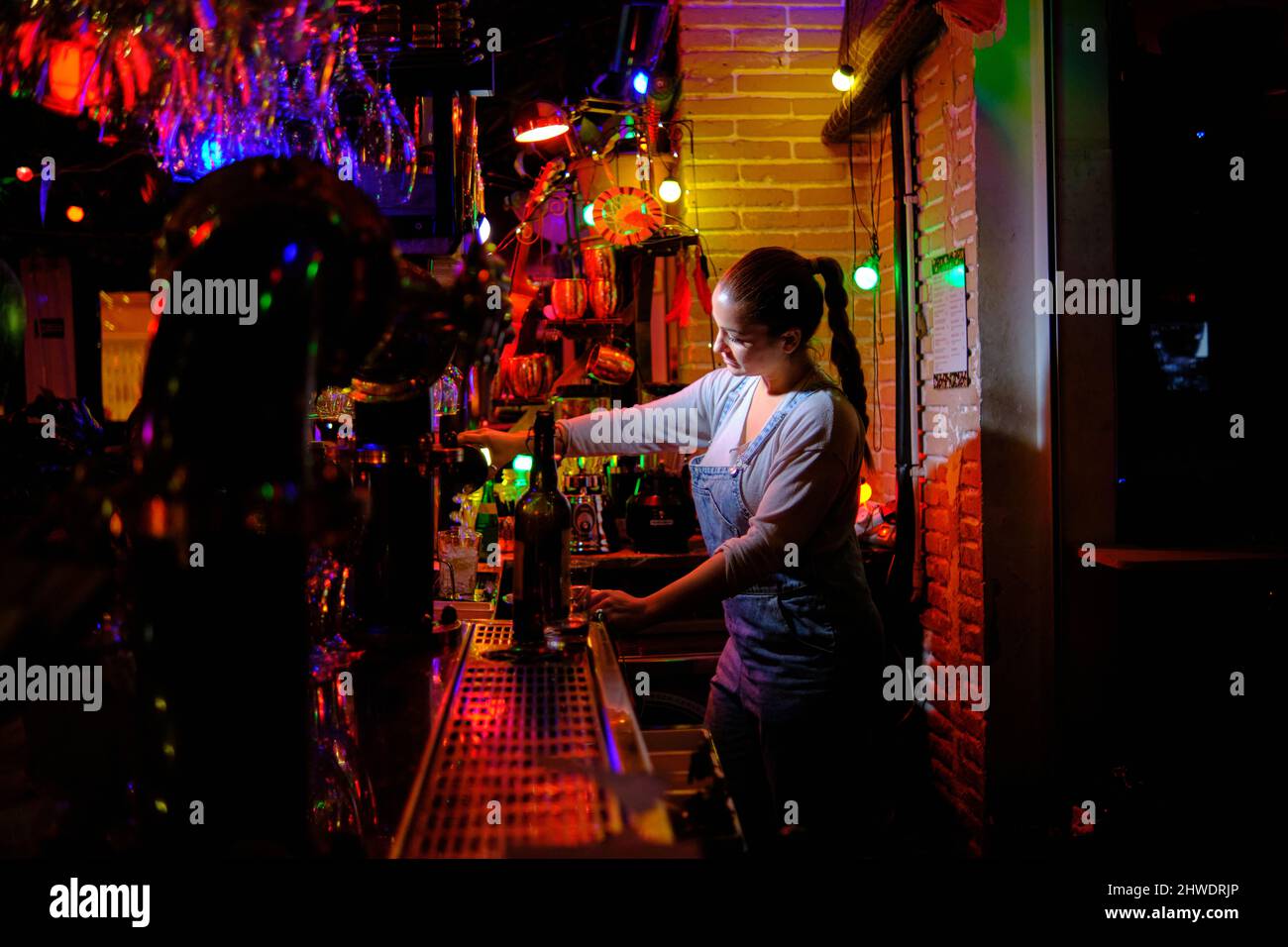 Die Barkeeperin bereitet einen Cocktail zu, während sie hinter dem Tresen einer Bar arbeitet. Stockfoto