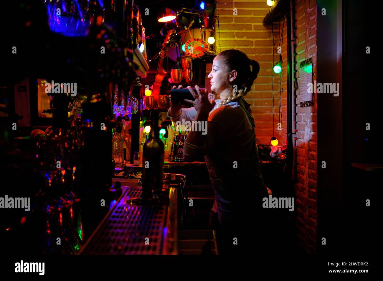 Die Barkeeperin mischt einen Cocktail in einem Shaker, während sie hinter der Theke einer Bar oder Kneipe arbeitet. Stockfoto