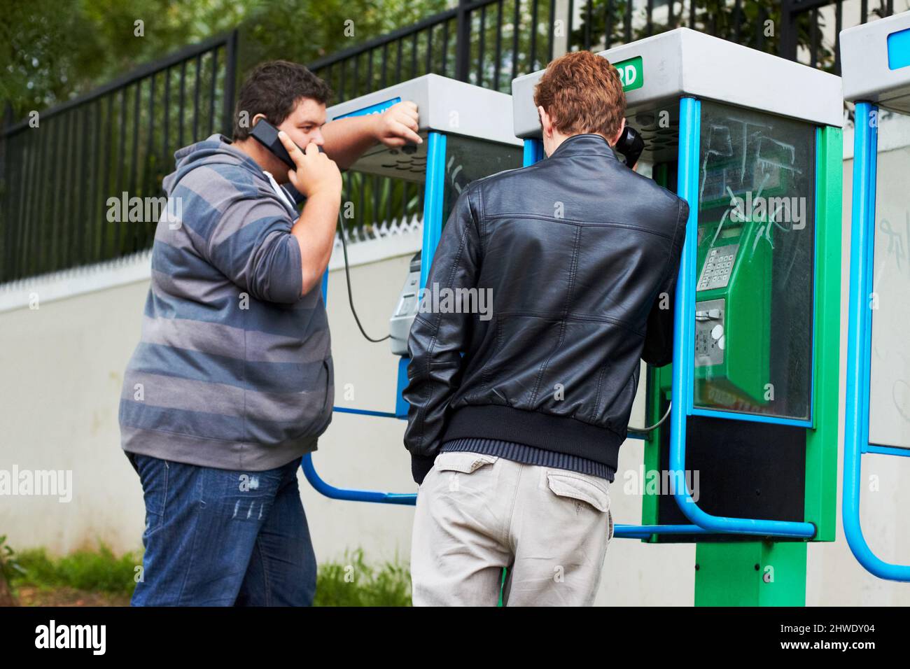 Nach Hause telefonieren. Zwei junge Männer, die von öffentlichen Telefonzellen aus telefonieren. Stockfoto