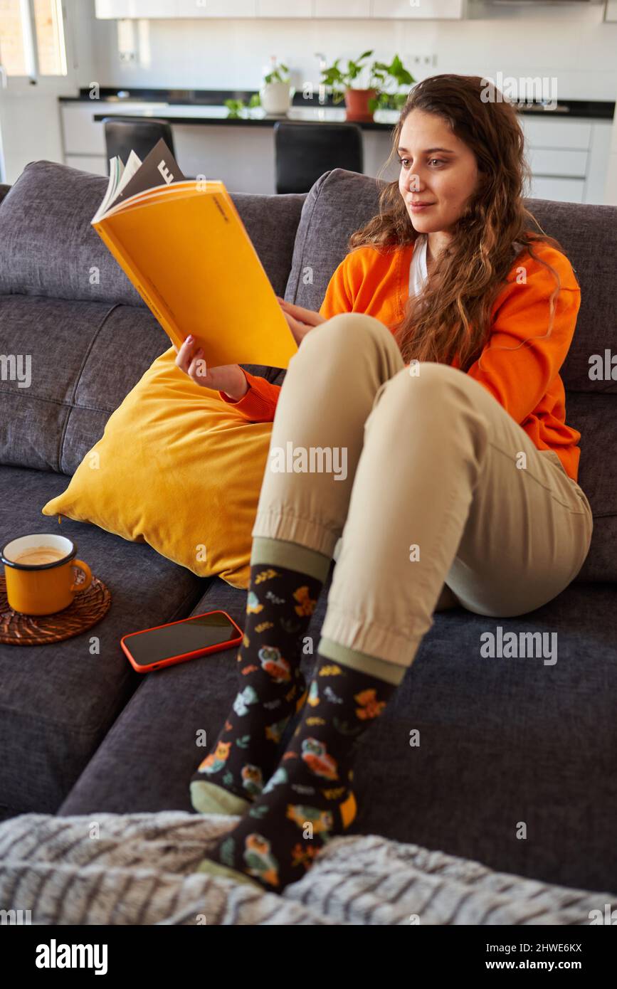 Junge Frau, die zu Hause ein Buch auf dem Sofa liest Stockfoto