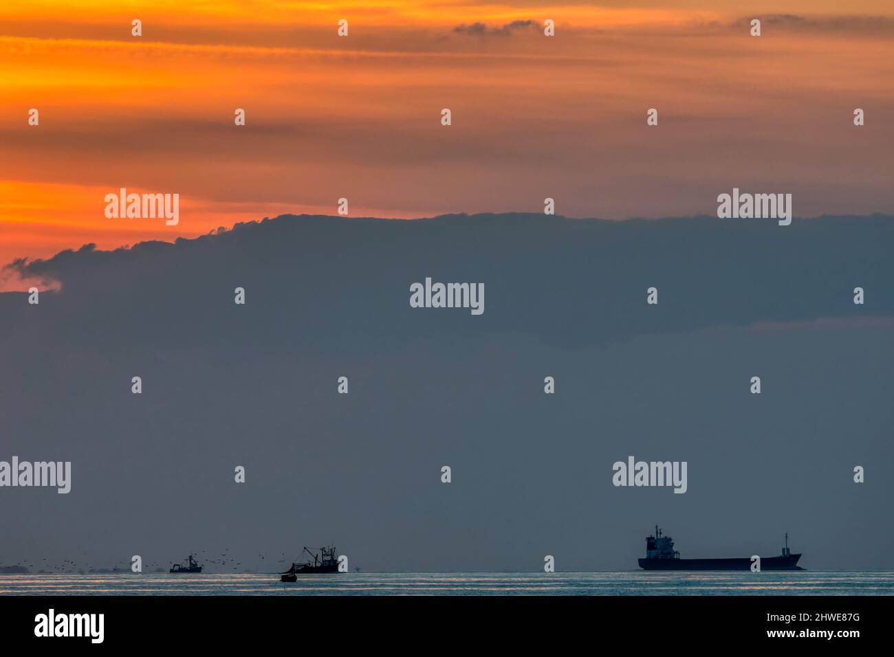 Frachtschiff und Fischerboote vor Sonnenuntergang über der Wash. Blick nach Westen von Norfolk Küste. Stockfoto