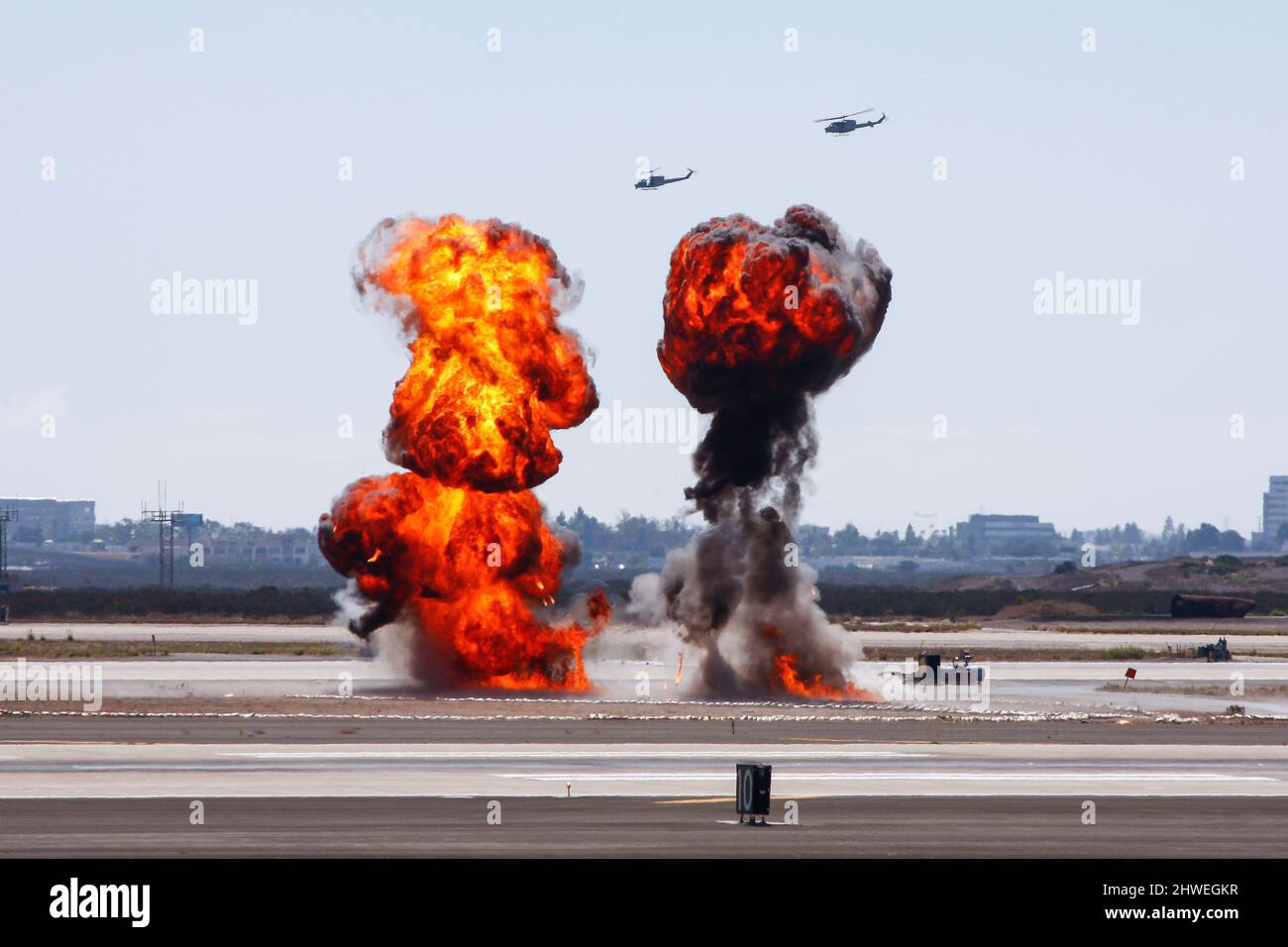 Bombenexplosion auf einem Flugplatz mit Kampfhubschraubern im Hintergrund in der Luft Stockfoto