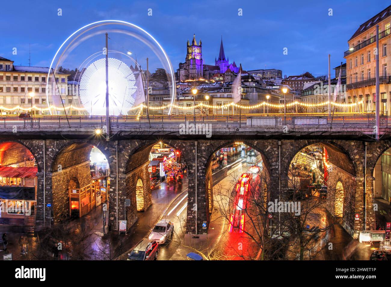 Blick auf die Kathedrale Notre-Dame und den Grand Pont in Lausanne mit dem Weihnachtsmarkt unter und hinter der Brücke. Das Riesenrad ist ein neuerer Sturm Stockfoto