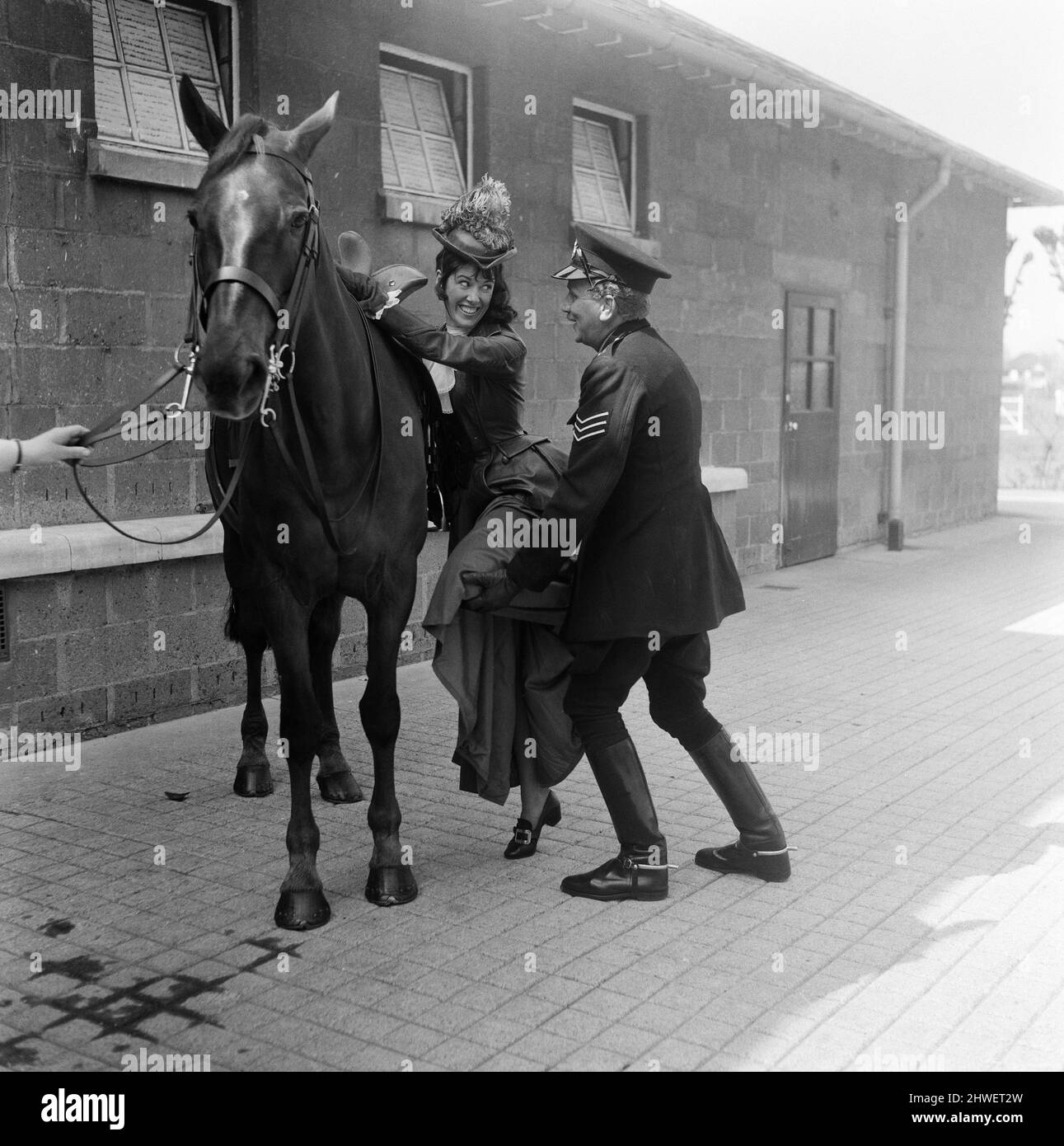 Sgt. David Lewis von Hammersmith unterstützt Susan Strank, eine der Moderatoren der Fernsehsendung „Magpie“, auf ihrem Pferd Quest. Zum ersten Mal seit 1829 hat der Kommissar der Mounted Police sein exklusives Vorrecht abgetreten, die Pferde zu nennen, die für Imber Court, die Metropolitan Police Mounted Branch Training Establishment, gekauft wurden. Die Zuschauer des Programms Magpie von Thames Television wurden gebeten, Namen für die sechs Pferde vorzuschlagen, die kürzlich von Imber Court gekauft wurden. 5. Mai 1970. Stockfoto