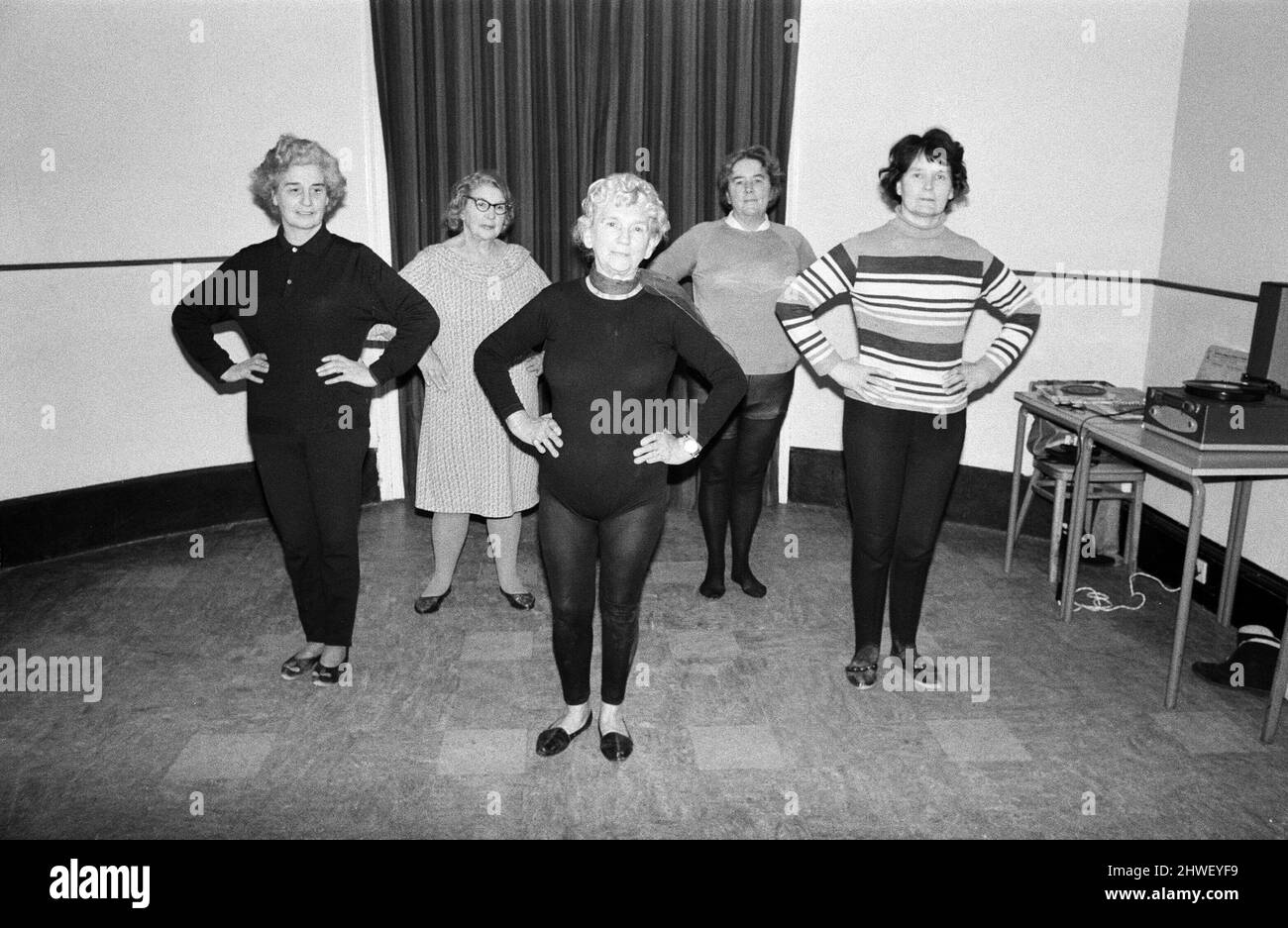 Cornwalls erstaunlichste Großmutter, Mrs Mary Wyatt (75 im April nächsten Jahres), tanzt sich in das neue Jahrzehnt der 1970s, bekleidet mit schwarzen Tanzstrumpfhosen, die einer Klasse von Frauen zeigen, wie sie energische und athletische Arm- und Beinstrecken zur Musik machen. Frau Wyatt hielt ihre erste Keep Fit-Klasse der 1970s in den Gemeinschaftsräumen im Guildhall in St. Ives, Cornwall. 2.. Januar 1970.Cornwalls erstaunlichste Großmutter, Mrs Mary Wyatt (75 im April nächsten Jahres), tanzt sich in das neue Jahrzehnt der 1970s, bekleidet mit schwarzen Tanzstrumpfhosen, die einer Klasse von Frauen zeigen, wie sie energische und athletische Arm- und Beinstrecken bis zum Mus machen Stockfoto
