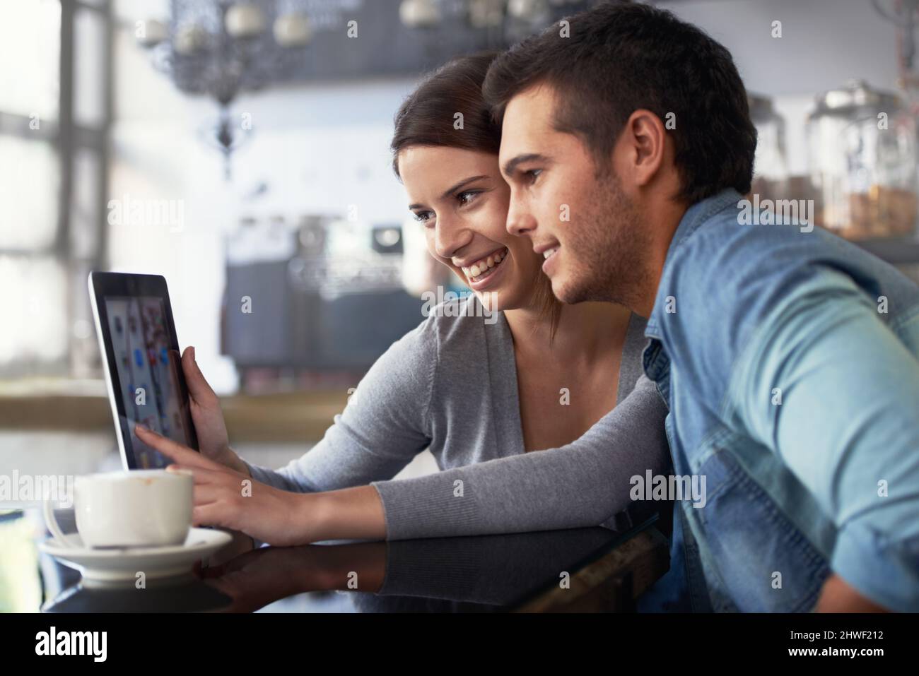 Zeigt ihm ihr Online-Fotoalbum. Aufnahme eines jungen Paares, das in einem Café auf ein digitales Tablet schaut. Stockfoto