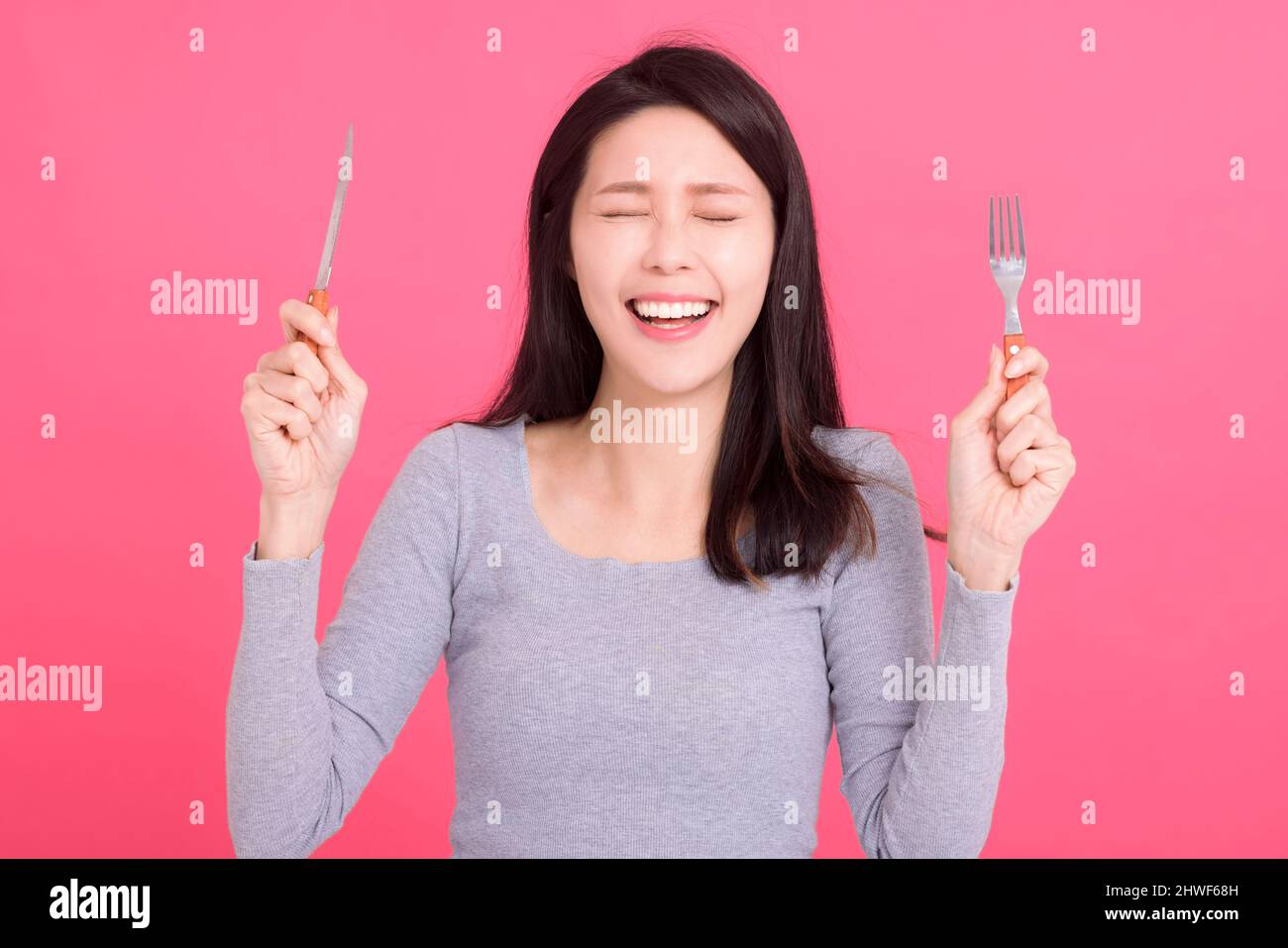 Aufgeregte junge Frau hält das Gabelmesser und genießt eine leckere Mahlzeit Stockfoto