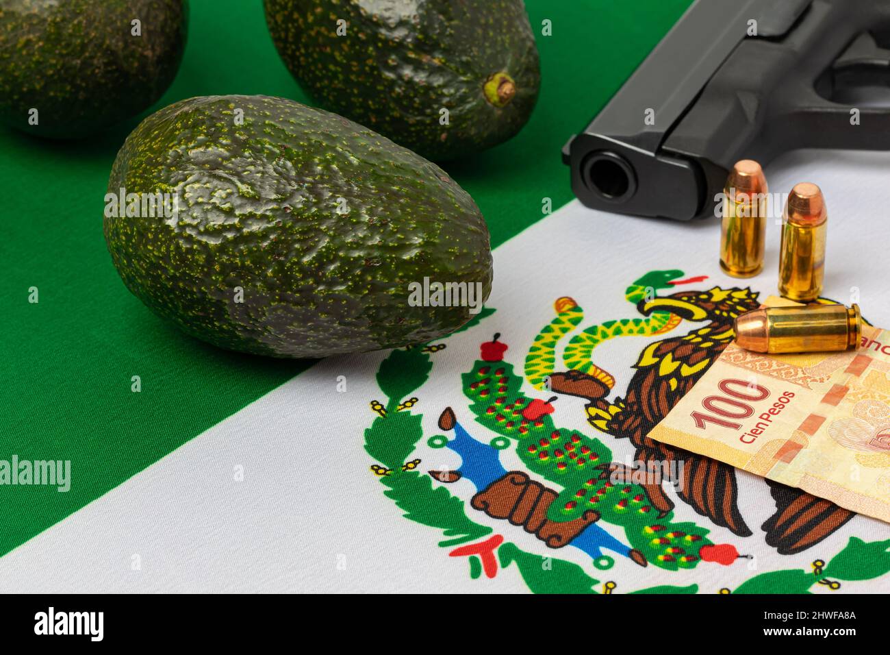 Avocados, mexikanische Flagge und Waffe. Erpressung, Gewalt und Kriminalität im mexikanischen Drogenkartell in der Avocado-Landwirtschaft. Stockfoto
