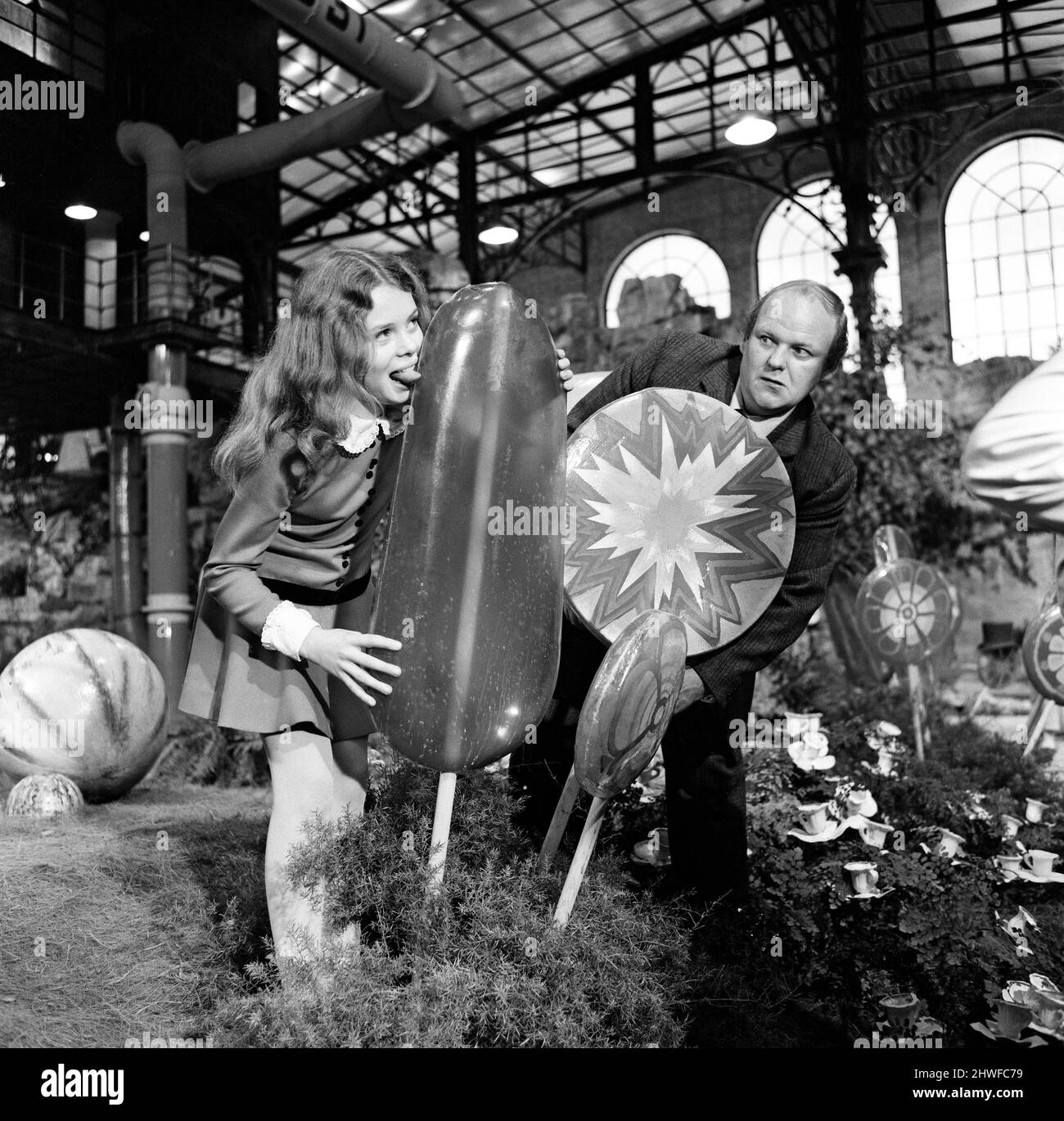 Der Schokoladenraum des Süßigkeitenmachers Willy Wonka mag nicht nur als eines der beeindruckendsten Studiosets, die jemals gebaut wurden, sondern auch als das vielleicht leckerste in die Filmgeschichte eingehen. Die immense Candy Room-Kulisse wurde auf der größten Klangbühne der Bavaria Studios in München errichtet, wo David L. Wolpers Produktion von „Willy Wonka und die Schokoladenfabrik“ nun gedreht wird. Das einzige britische Mädchen im Film, Julie Dawn, 12 Jahre alt, aus Guildford, schmeckt einen der riesigen Lutscher, die der britische Schauspieler Roy Kinnear, der ihren Vater spielt, beobachtet. 8.. Oktober 1970. Stockfoto