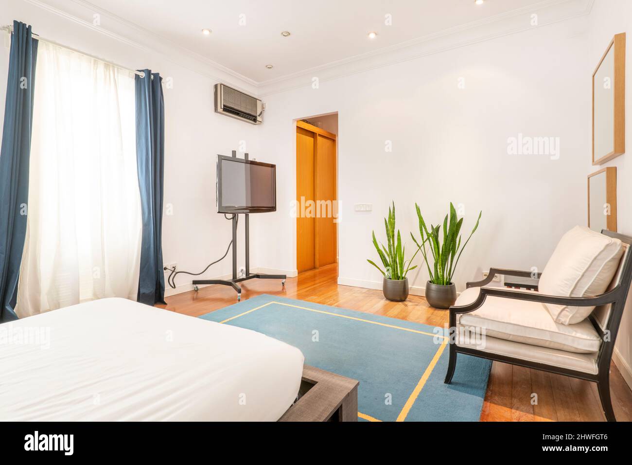 Schlafzimmer mit Kingsize-Bett und Sitzecke mit mobilem fernseher mit blauem Teppich auf Kirschholzboden Stockfoto