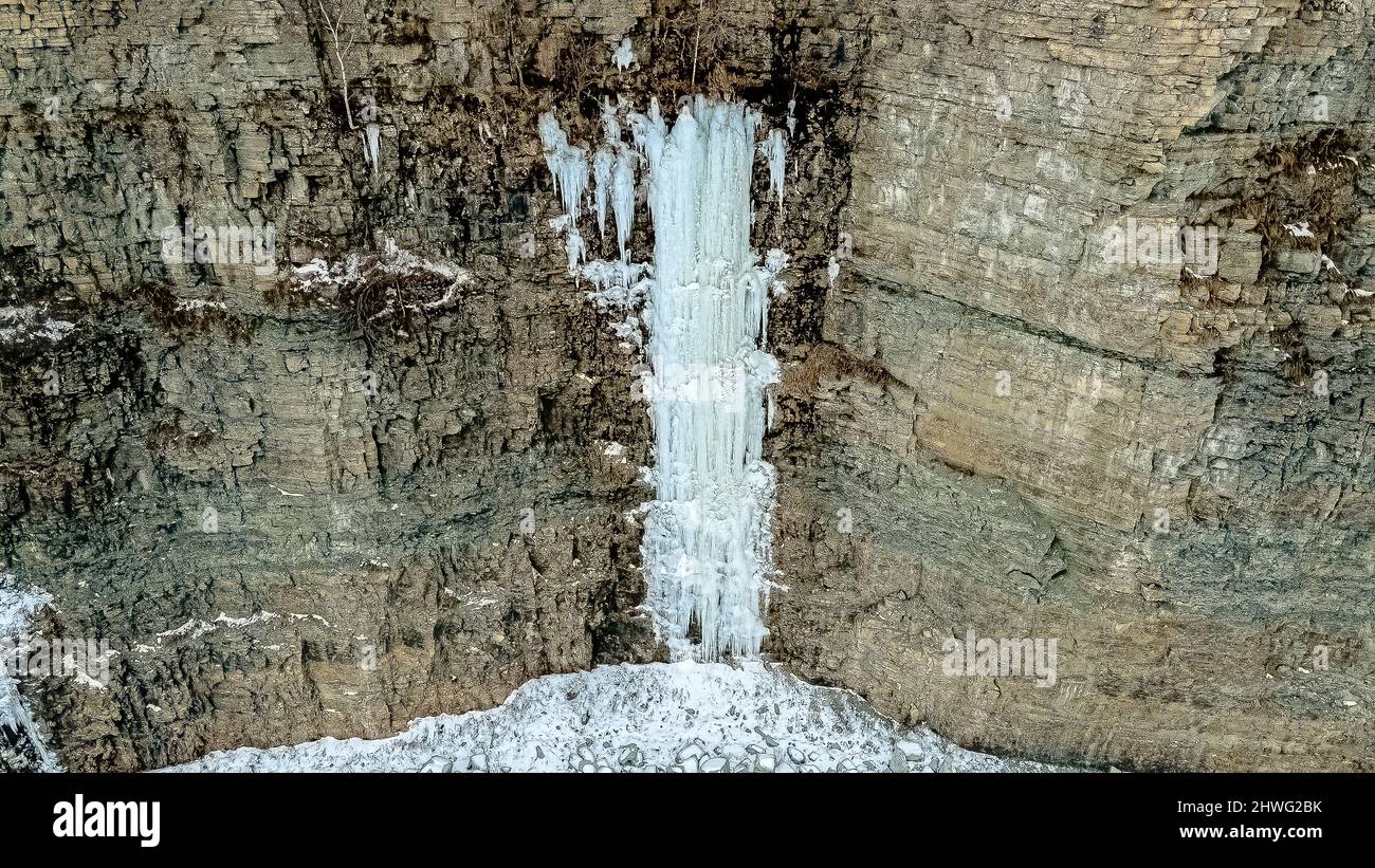 Eis- und Schneeformationen an den Wänden eines Steinbruchs. Der Schnee schmilzt auf dem Land darüber und ergießt sich über die Wände und friert, wodurch majestätische Formationen entstehen. Stockfoto