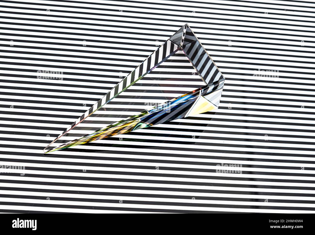 Glaspyramidenprisma mit farbenfroher Lichtreflexion auf weißem horizontalen Streifen auf schwarzem Hintergrund Stockfoto