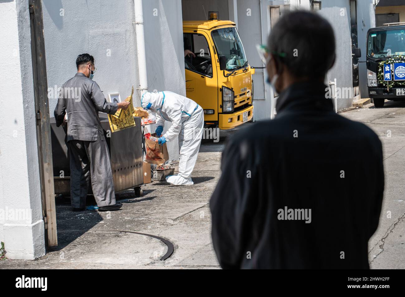 Ein Familienmitglied beobachtet, wie ein privater Leichengehege-Arbeiter in PPE den Leichnam eines covid-19-Opfers für die Beerdigung in der öffentlichen Leichenhalle von Victoria vorbereitet. Mit dem jüngsten Anstieg der Todesfälle aufgrund des Omicron-Ausbruchs in Hongkong sind die örtlichen Leichenhallen in der Lage, und die Regierung verlässt sich auf Krankenhäuser und private Leichenhäuser, um Hilfe zu erhalten. Am 5. März 2022 sind in der letzten Welle 1561 Menschen gestorben, was die Gesamtzahl der bekannten COVID-19-Todesfälle in Hongkong auf 1774 brachte. Die meisten Todesfälle wurden bei älteren Menschen verzeichnet, von denen viele entweder nicht oder nicht vollständig geimpft waren. Stockfoto