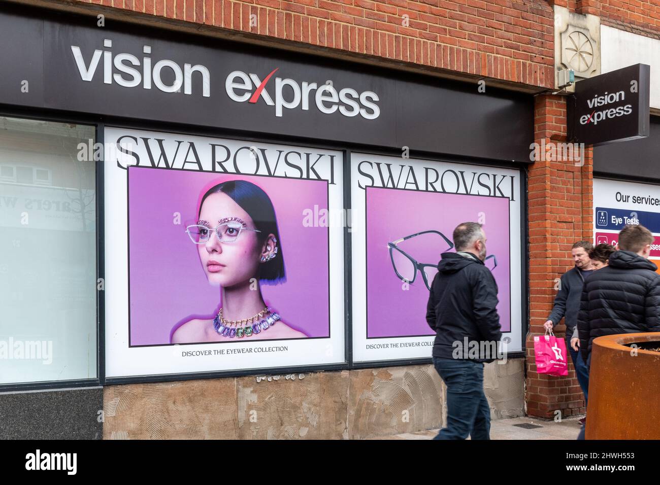 Menschen, die an Swarovski-Anzeigen in einem Optikergeschäft von Vision Express vorbeigehen, im Stadtzentrum von Camberley, Surrey, England, Großbritannien Stockfoto