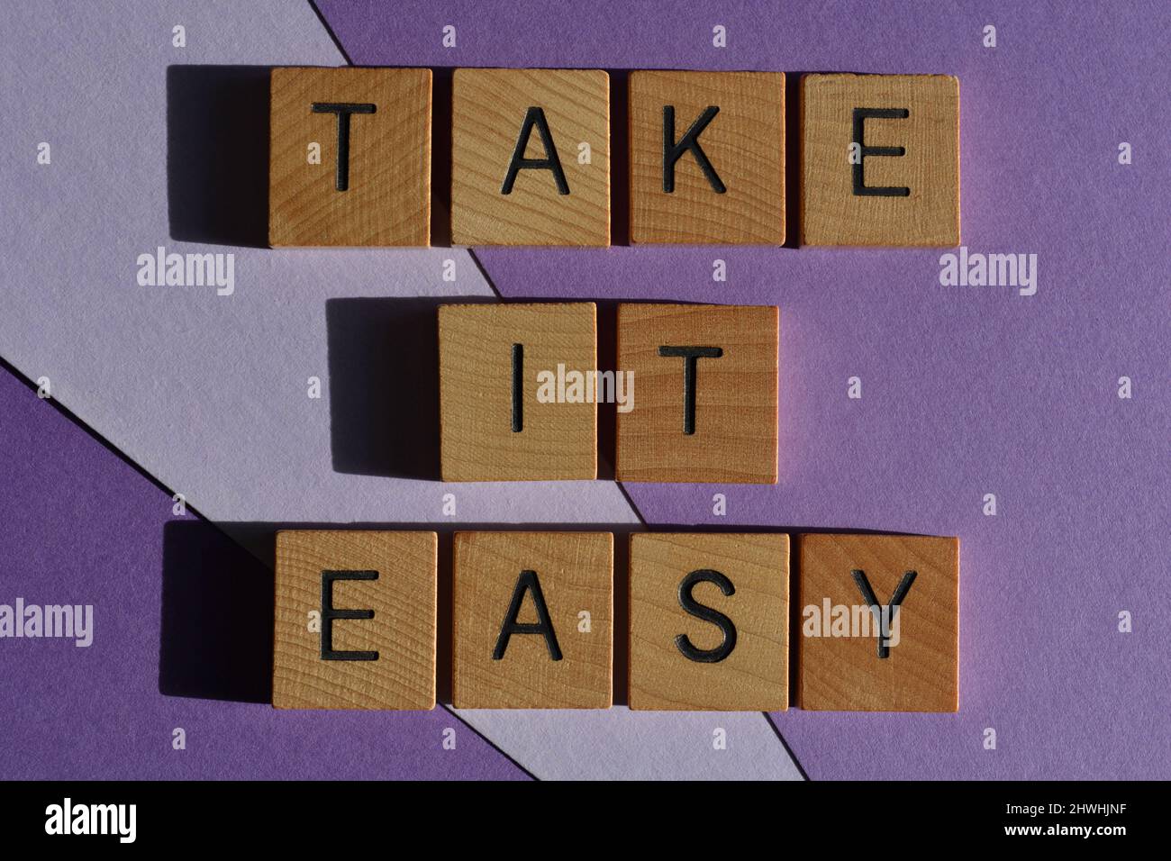 Take IT Easy, Wörter in Holzbuchstaben isoliert auf violettem Hintergrund Stockfoto