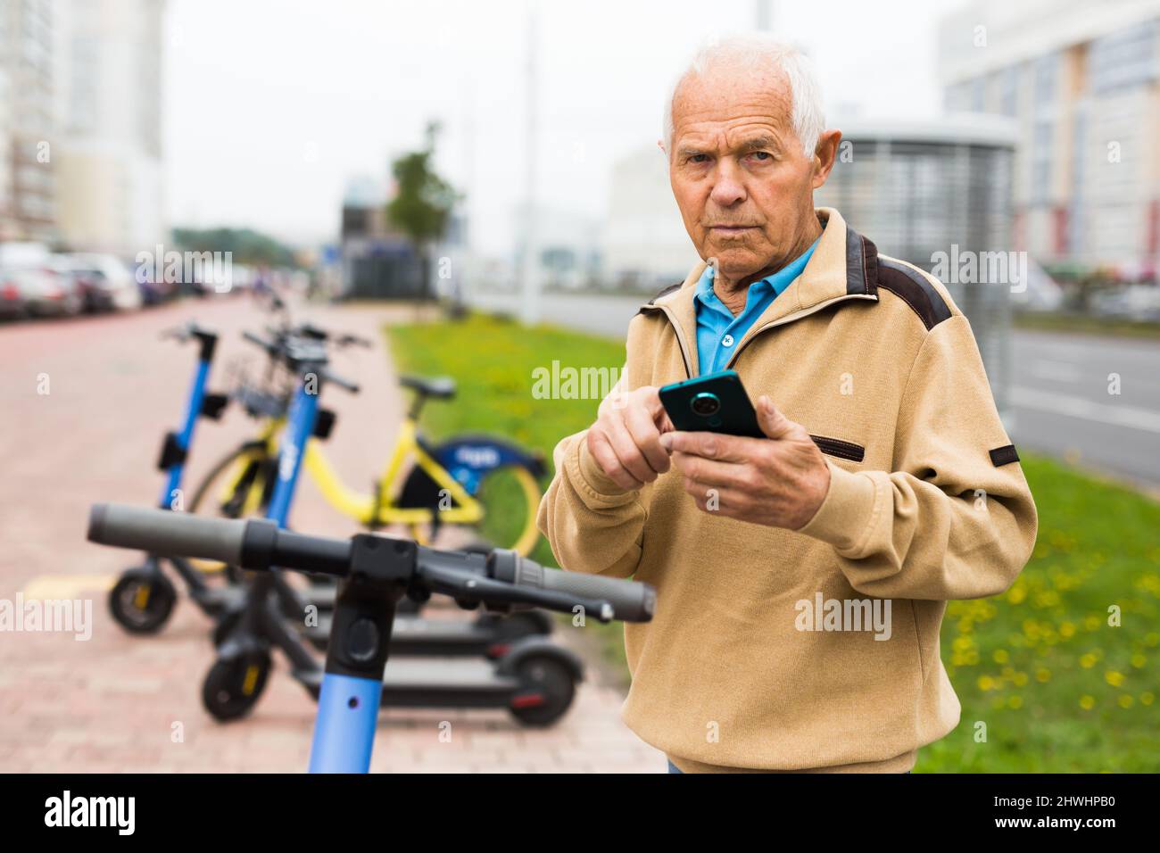 Älterer Mann mietet sich einen Elektroroller mit dem Mobiltelefon Stockfoto