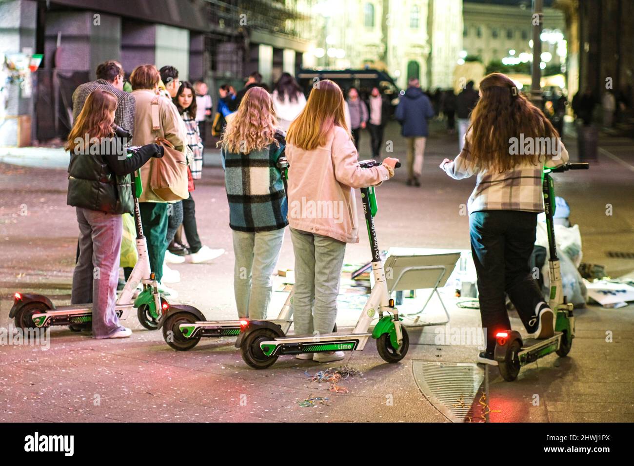 Mailand, Italien - Junge Frauen mit Elektrorollern machen einen Stopp, um einen Straßenkünstler bei der Arbeit zu beobachten Stockfoto