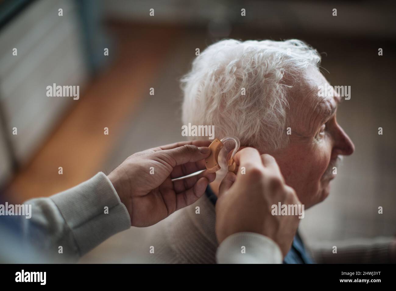 Nahaufnahme der Hand des Pflegepersonals, die ein Hörgerät in das Männerohr des Senioren einführt. Stockfoto